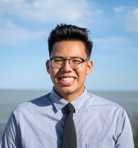 Headshot of Ethan Chiu, a Chinese/Mexican male with medium brown skin, short black hair and glasses, wearing a grey button down shirt and black tie.