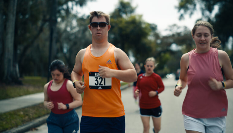 Image showing four runners, with the runner at the front in an orange vest that features bib number 321.